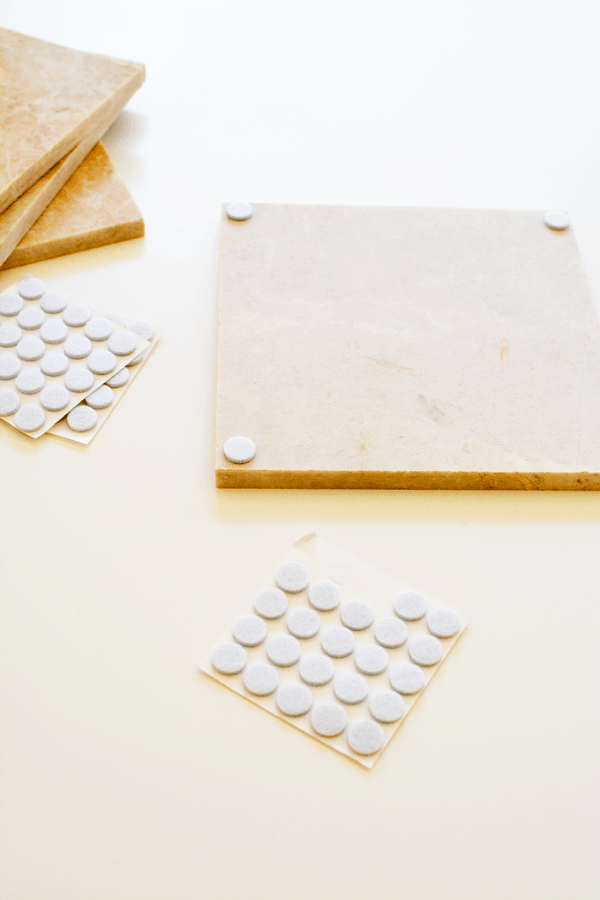 A tile on a table, upside down, with stick-on felt pads on each corner.