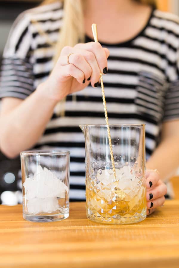 A woman mixing a cocktail in a drink pitcher. 