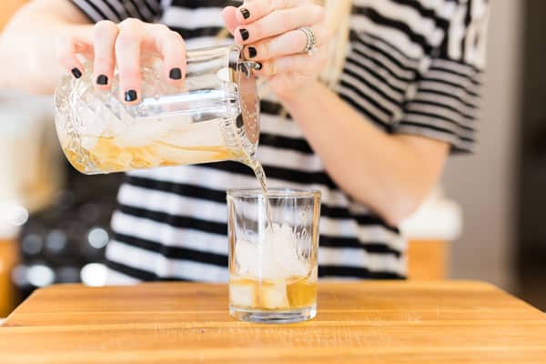 Woman pouring a Pine Old Fashioned into a cocktail glass over ice. 