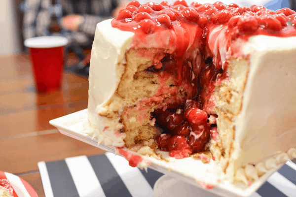 A close up of cherry pie filling spilling out of layers of vanilla cake with cherry pie baked in.