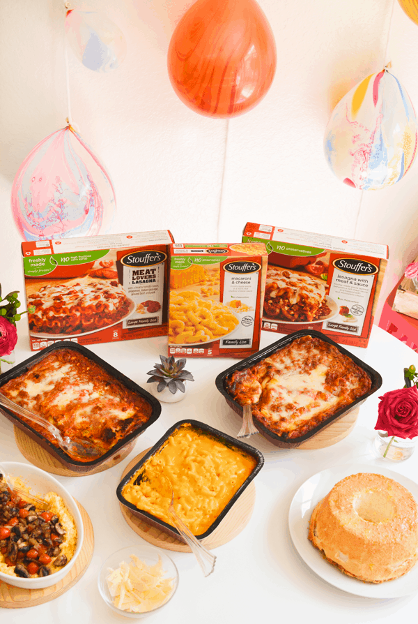 A table with party food including family sized frozen lasagnas and macaroni and cheese along with the Stouffer's packaging. 