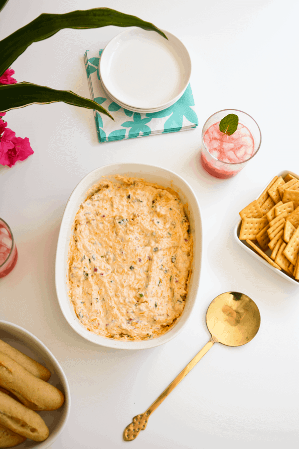 Baking dish with dip on a party table next to crackers and drinks.