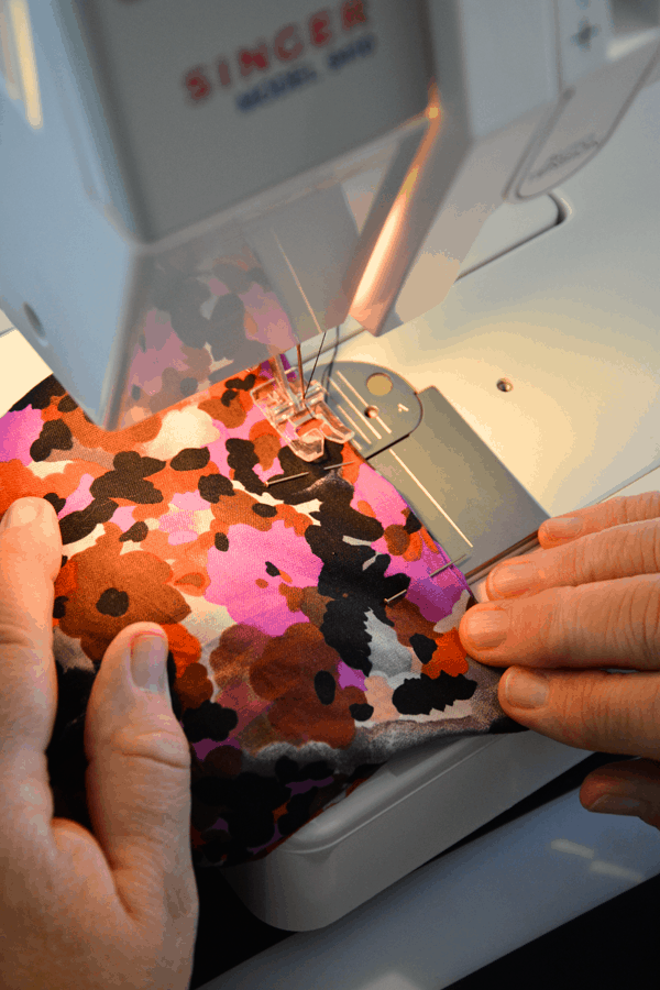 Woman sewing pieces of fabric with straight pins on a sewing machine. 