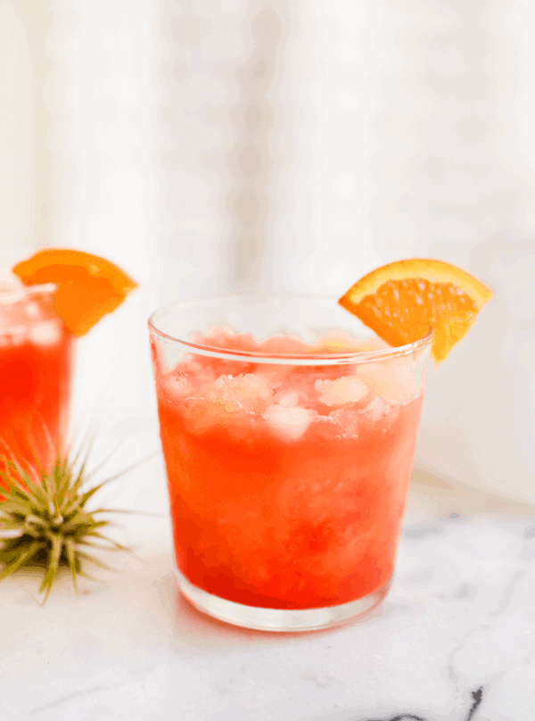 Glass full of a pink and orange Vodka Sunrise cocktail on a table. 