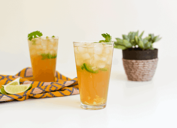 Side view of two glasses with ice and a Tequila Mule with Jalapeno cocktail on a table. 