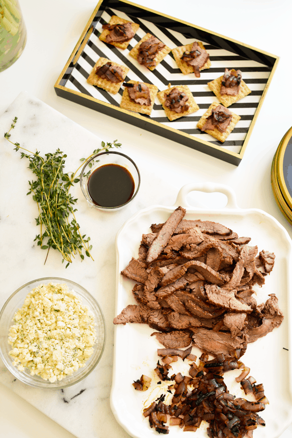 A tray of Triscuit Appetizers with steak and blue cheese on a table next to more ingredients to make them.