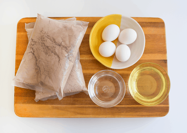 A bag of boxed brownie mix and the ingredients to make a brownie birthday cake on a wooden cutting board.