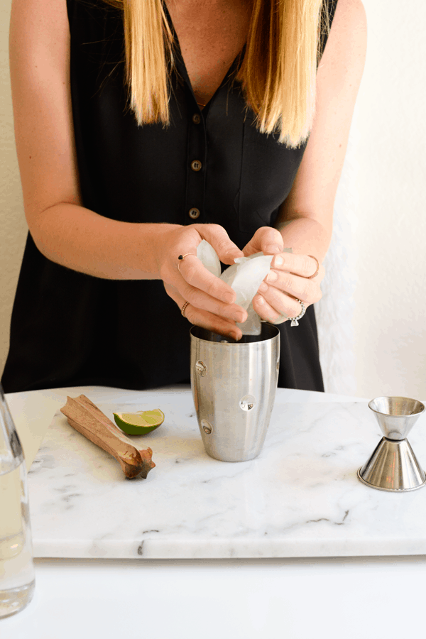 Woman adding ice to a cocktail shaker. 