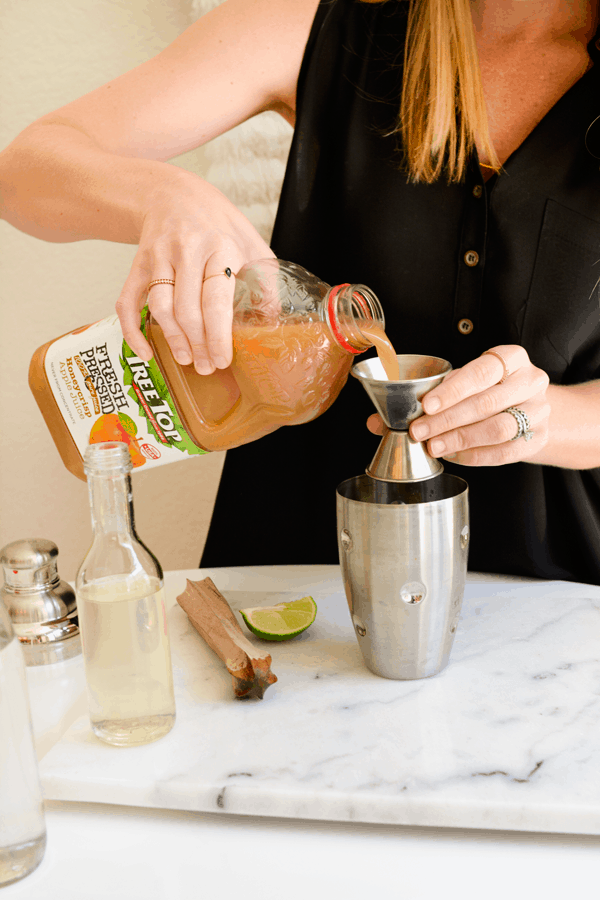 Woman measuring apple juice into a cocktail shaker.