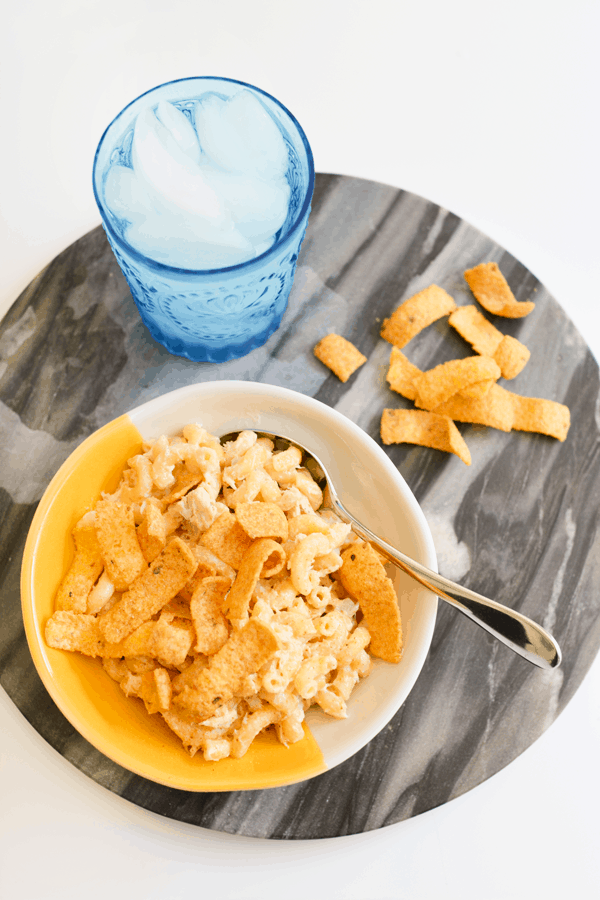 A yellow and white bowl holding elbow noodles tossed with mayonnaise and tuna and topped with corn chips. 