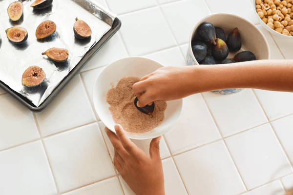 Child dipping figs in a bowl of sugar and spices.