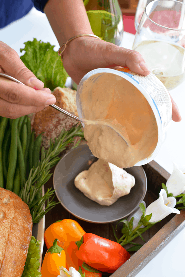 Woman spooning a premade dip into a serving bowl. 