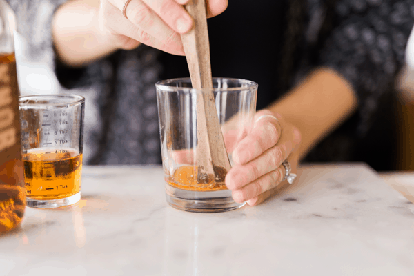 Woman using a muddler to break up a bitters soaked sugar cube. 