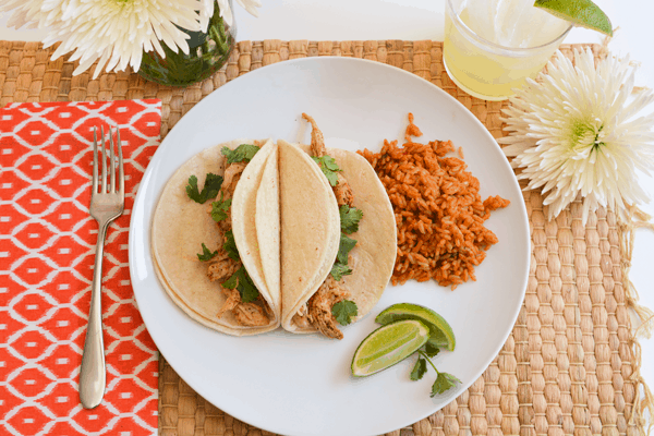 Shredded chicken tacos on a plate with a side of rice.