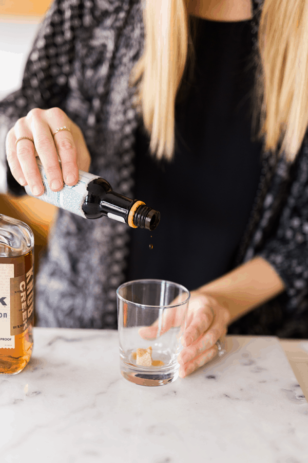 Woman adding bitters to a sugar cube in a cocktail glass.