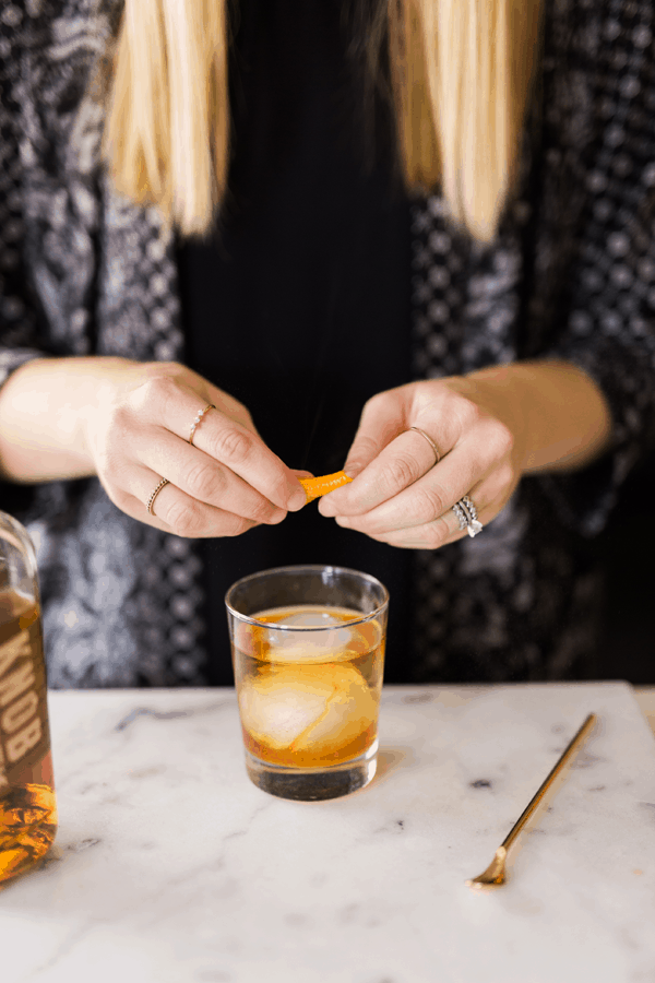 Woman adding an orange peel garnish to a Knob Creek Old Fashioned. 