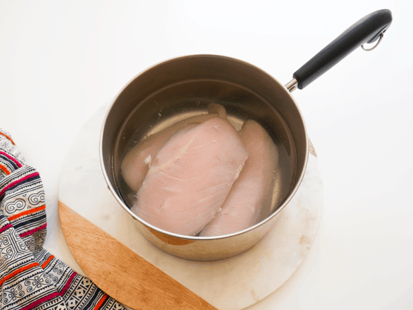 Raw chicken breasts in water in a saucepan.
