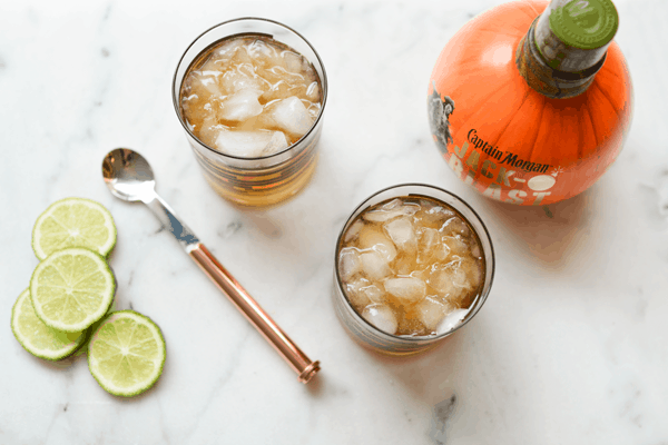 Overhead shot of two cocktail glasses with a Pumpkin Moscow Mule and a bottle of pumpkin rum.