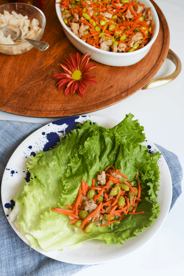 A lettuce leaf with teriyaki ground turkey stir fry next to a wood tray with the rest of dinner.