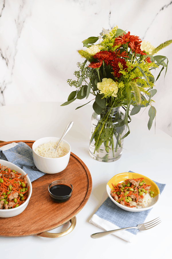 White table with a wood tray and ground turkey stir fry in a bowl.