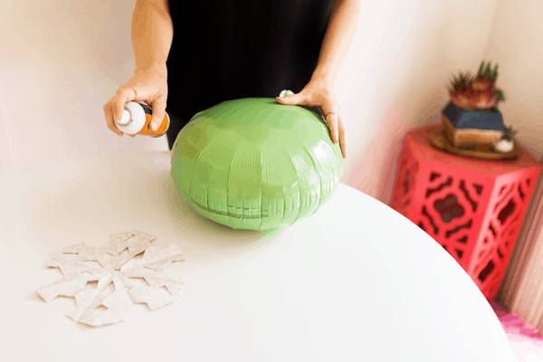 Woman using spray adhesive on a snowflake while holding a balloon with her other hand. 