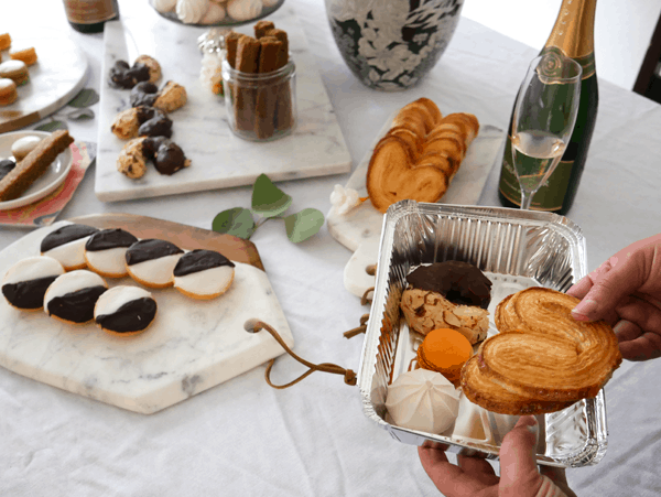 A woman putting cookies in a tin to-go box next to a party table for a cookie exchange party.