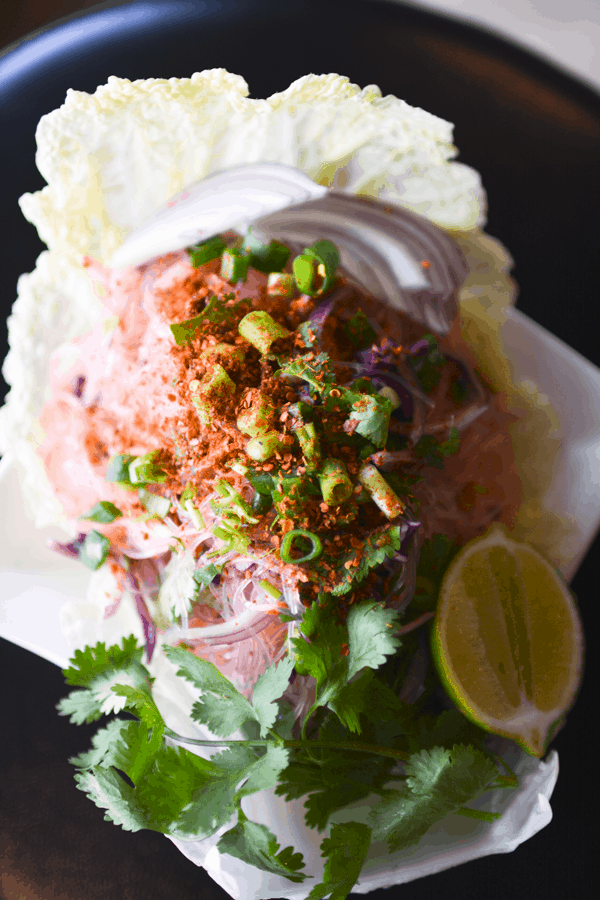 Close up of a Glass Noodle Salad on a white plate topped with chile flakes and chopped green onions.