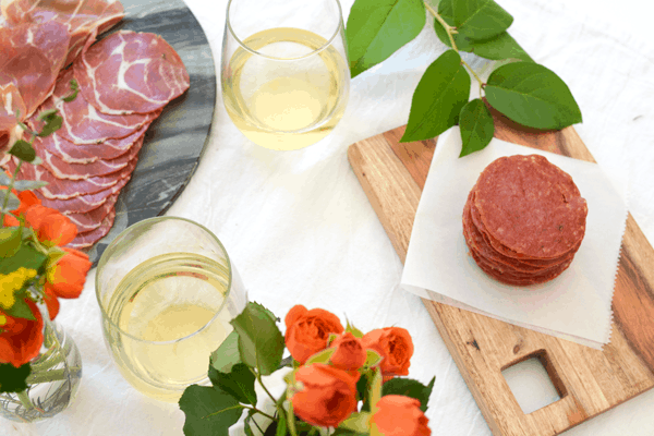 Top down view of a table top set with wine glasses, greenery and flowers, and baked salami chips.