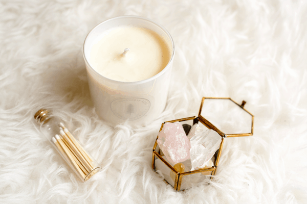 A white candle, a small glass jar of candles and a small glass container with crystlas on a white furry carpet are great for how to make your home feel more like a spa.