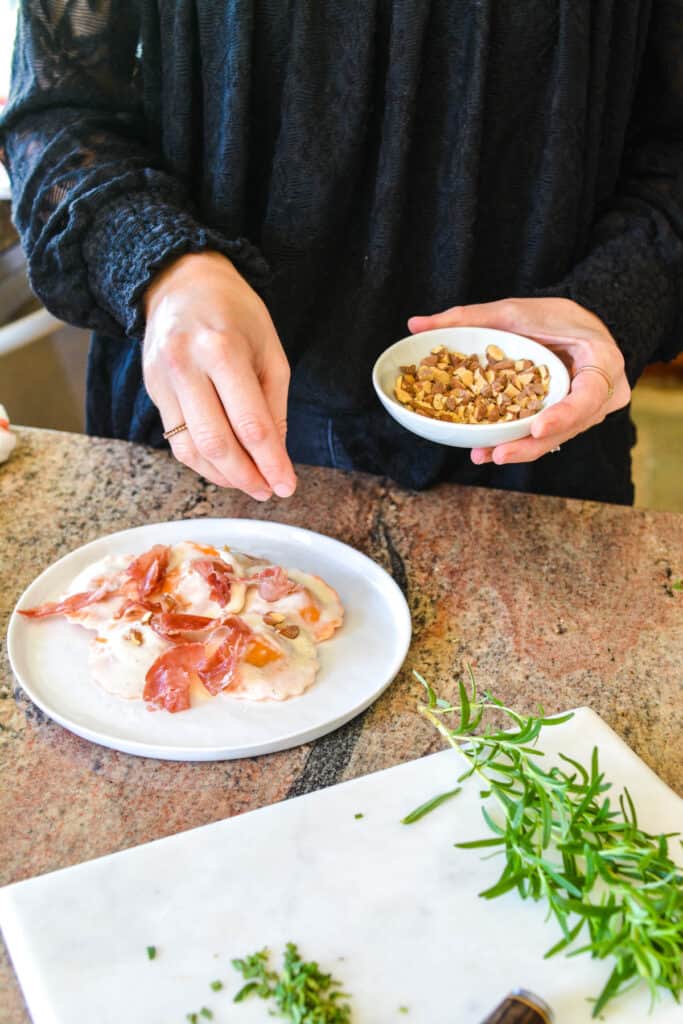 A woman adding chopped almonds to a plate of ravioli.