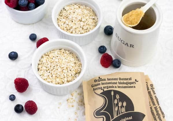 Dry oats in a few ramekins on a table next to packets of oatmeal, sugar and fresh berries.