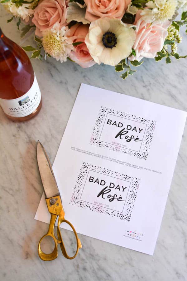 A sheet of printable labels on a counter next to scissors and a bottle of rosé.