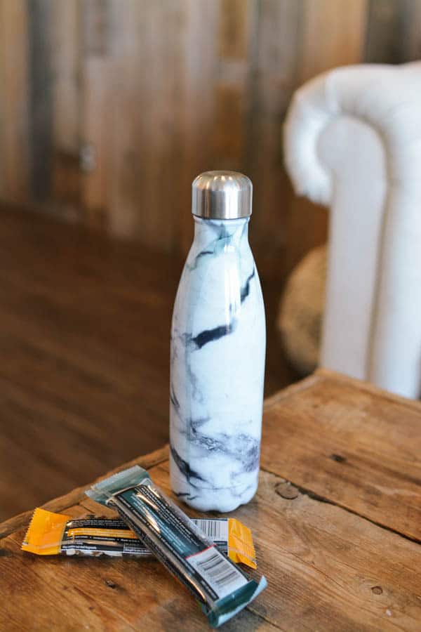 A refillable water bottle and some protein bars on a table for a mom getaway. 