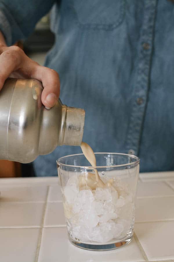 Woman pouring a Cold Brew White Russian over ice in a cocktail glass. 