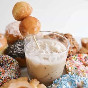 A Coffee White Russian in a short cocktail glass with a skewer holding two donut holes.