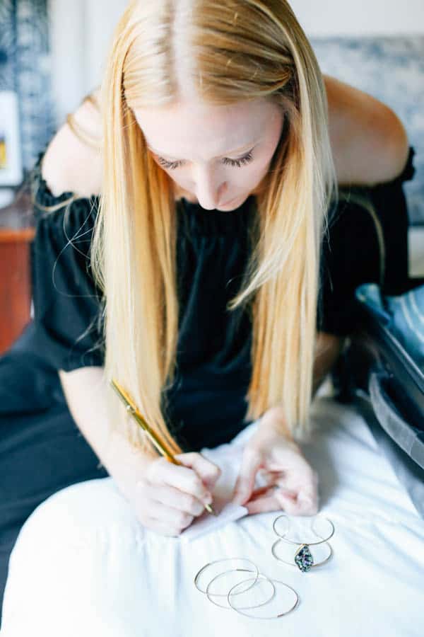 Woman writing on post it notes to organize how she'll wear her jewelry on vacation.