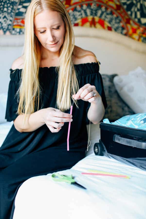 Woman putting a necklace into a straw to keep it from tangling while traveling.