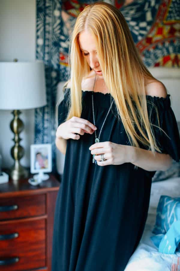 Woman fixing her necklace that she's wearing with her dress. 