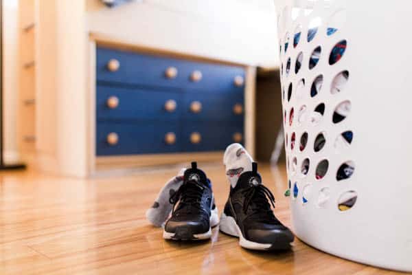 Sneakers on the ground next to a dirty clothes hamper. 