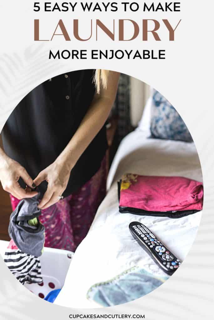 A woman folding laundry next to a bed with a TV remote on the bed.