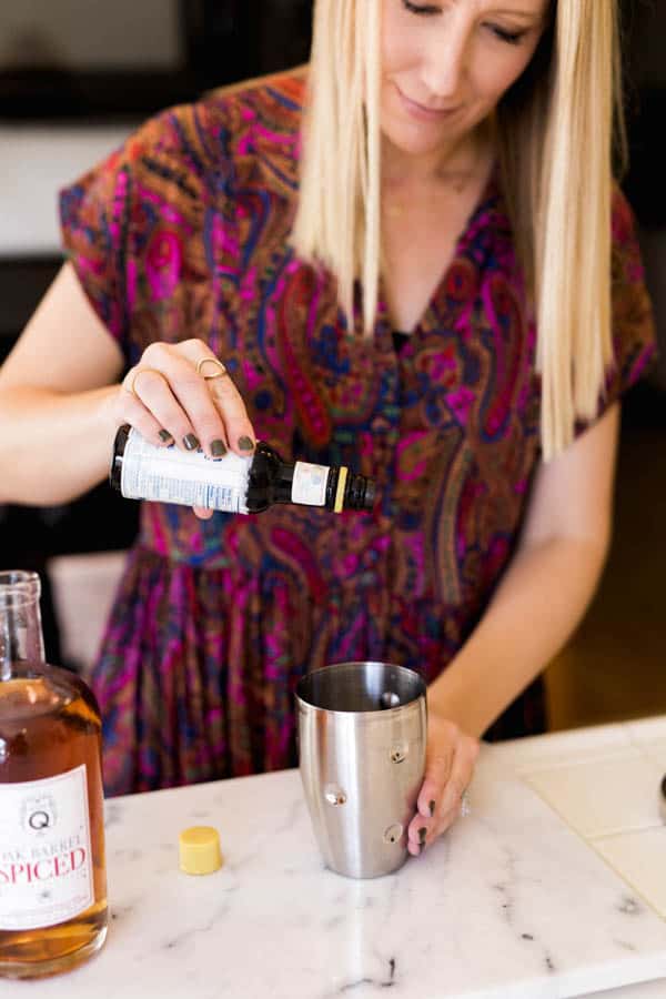 Woman adding a few drops of bitters to a cocktail shaker. 