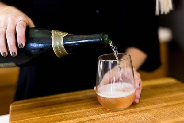 Woman pouring champagne into a glass of kombucha.