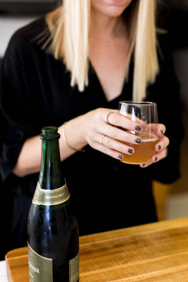 Woman holding a kombucha mimosa with a bottle of champagne in the foreground.