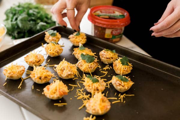 Woman adding cilantro to the top of Chicken Taco Cups appetizers on a cookie sheet. 
