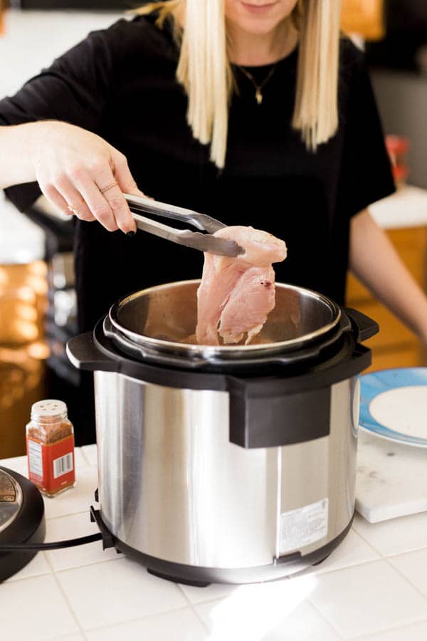 Woman adding chicken pieces to an Instant Pot.