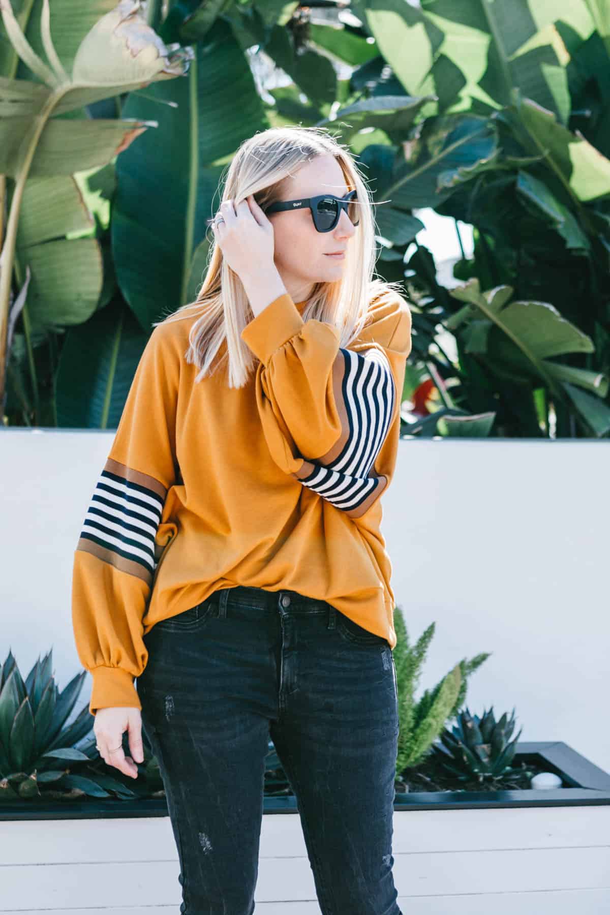 Woman standing outside in a mustard colored sweatshirt and black jeans with fresh Botox in her forehead.