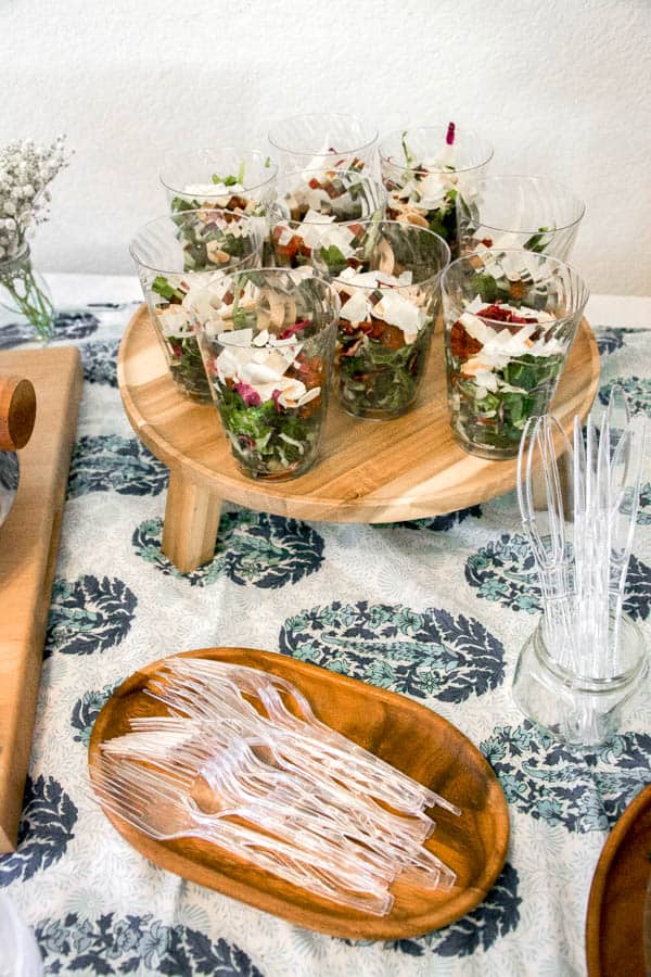 Salad in cups on a wood tray.