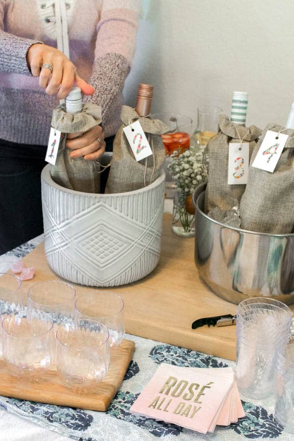 Woman opening a bottle of wine that sits on a table in a wine bucket.