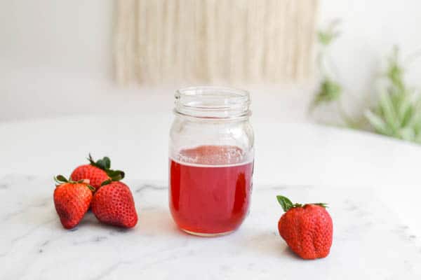 Strawberry simple syrup on a table next to some strawberries.