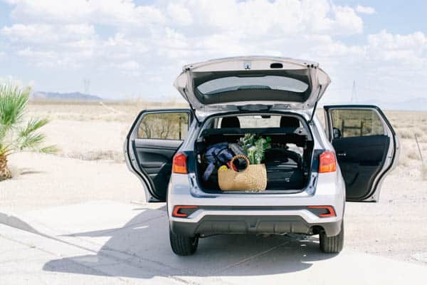 A car with the hatch  and doors open off the side of a road for a road trip. 